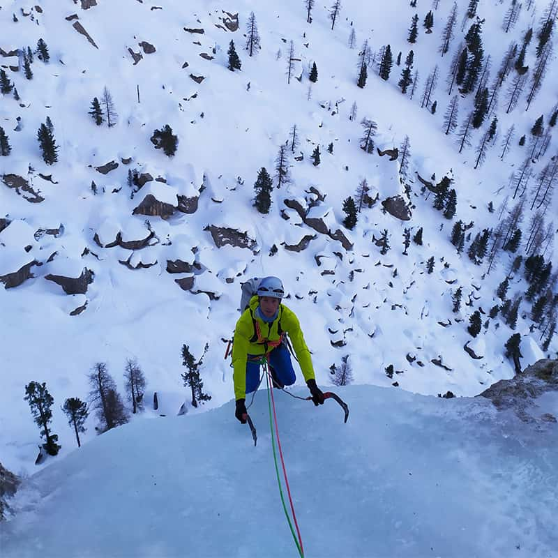 Un homme arrive en haut d'une cascade de glace avec ses deux piolets arrimés dans la glace.