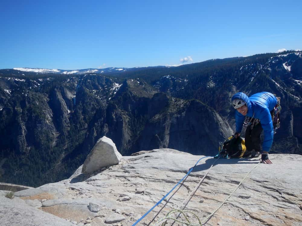 Alexandre Hénot sourit sur le bord d'une falaise, une chaine de montagnes s'étend à l'horizon.