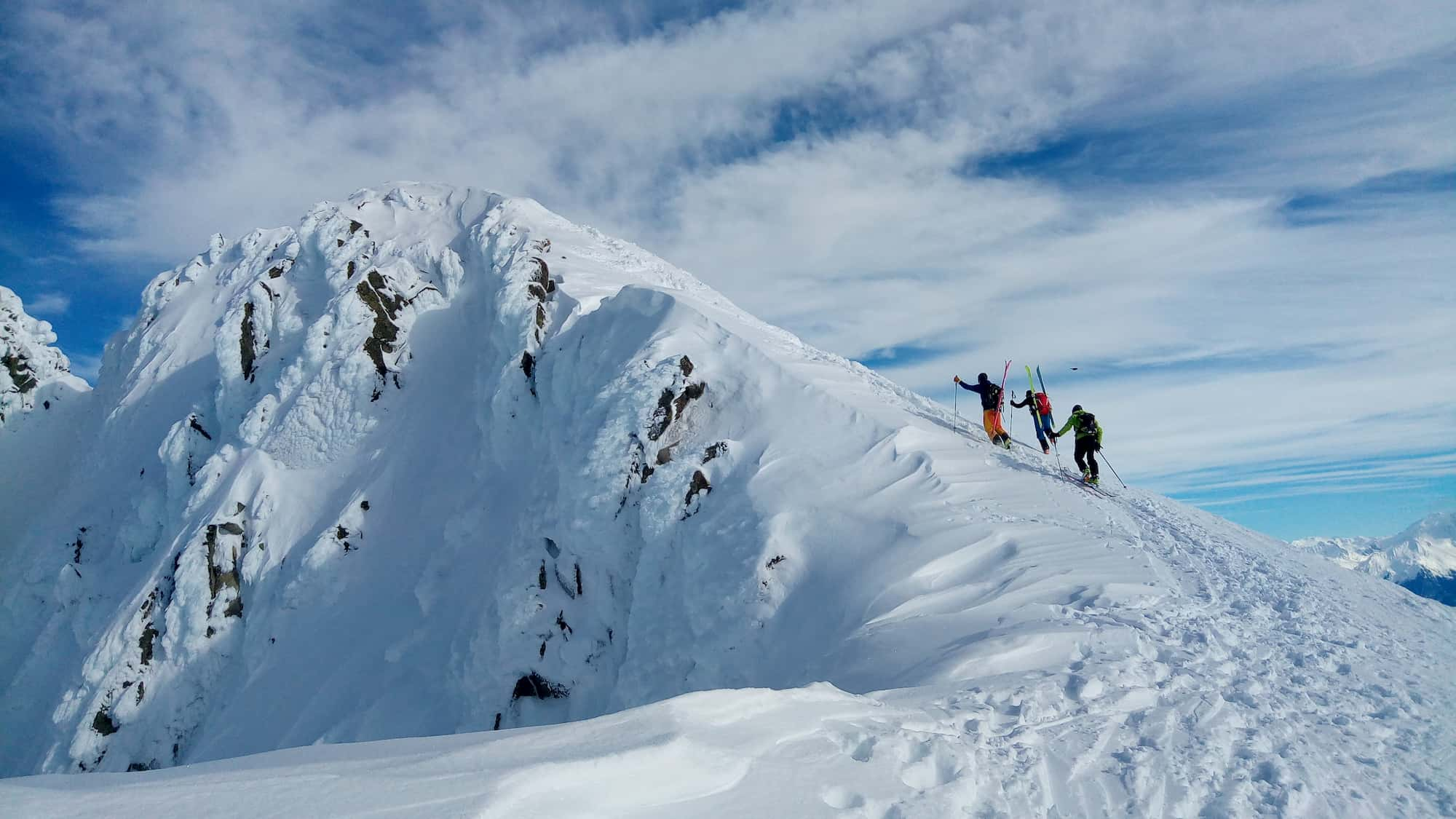 Une équipe de 3 personnes arrive au sommet d'une montagne enneigée.