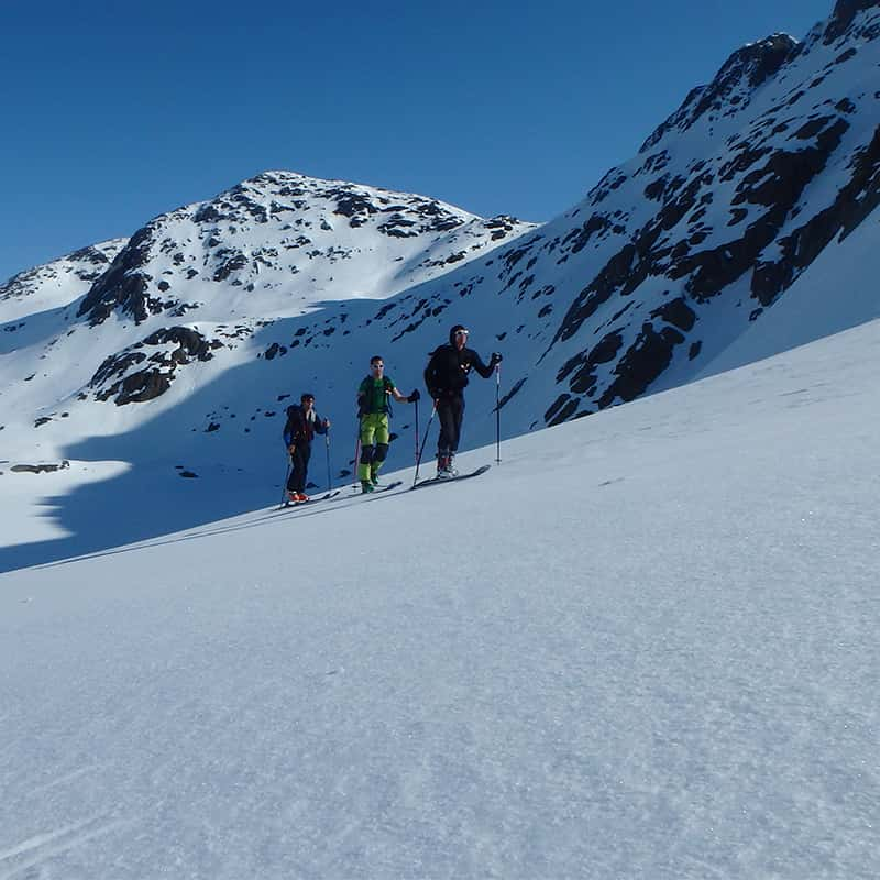 Trois personnes avancent en ski de randonnée le long d'une montagne.